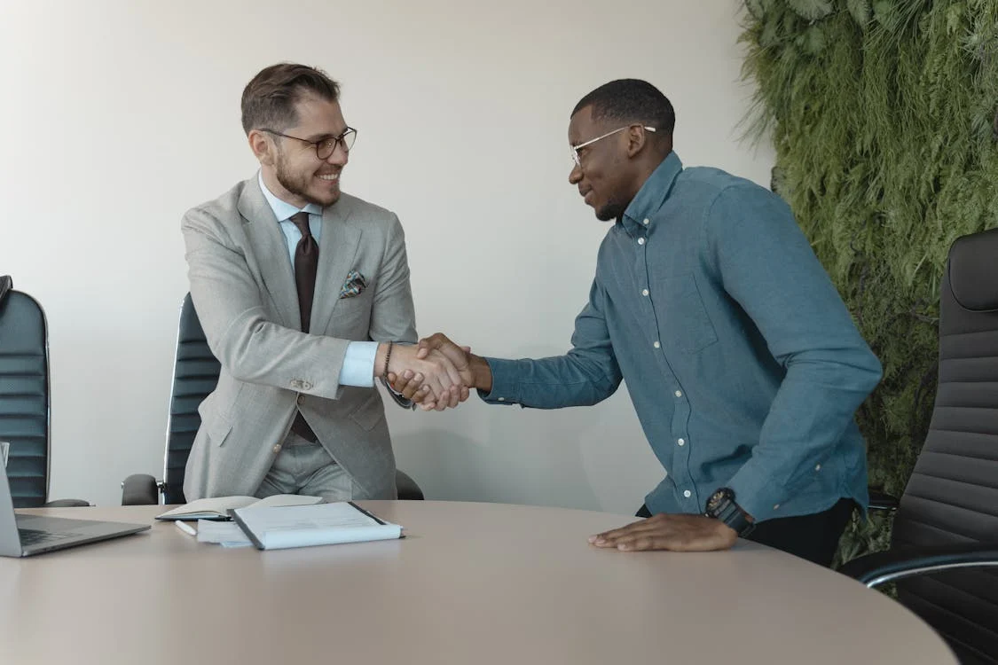 Dois homens se cumprimentando com um aperto de mãos, durante uma entrevista de emprego.