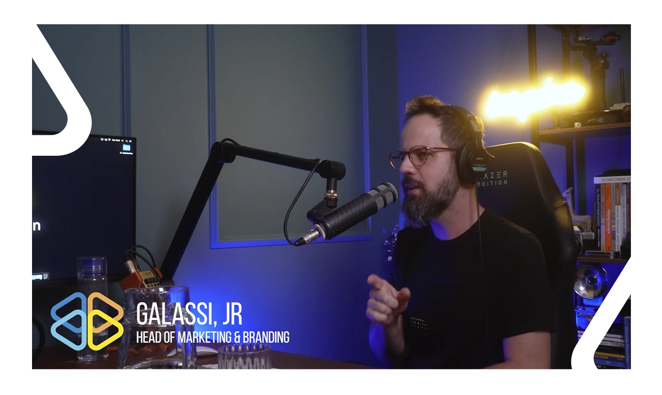 Homem branco, de óculos, cabelo castanho, bigode e barba, sentado em um estúdio de gravação de áudio